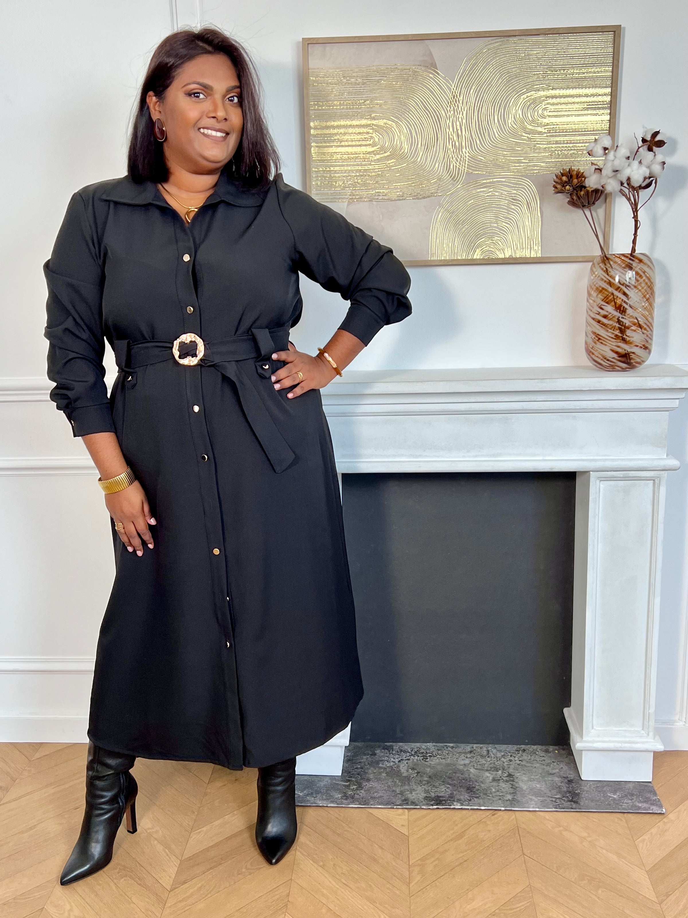 Cette robe longue noire grande taille, Agatha, allie élégance et confort. Dotée de manches longues et d’un col chemise, elle s’ouvre sur une série de boutons dorés tout au long du devant et aux manches, apportant une touche raffinée.