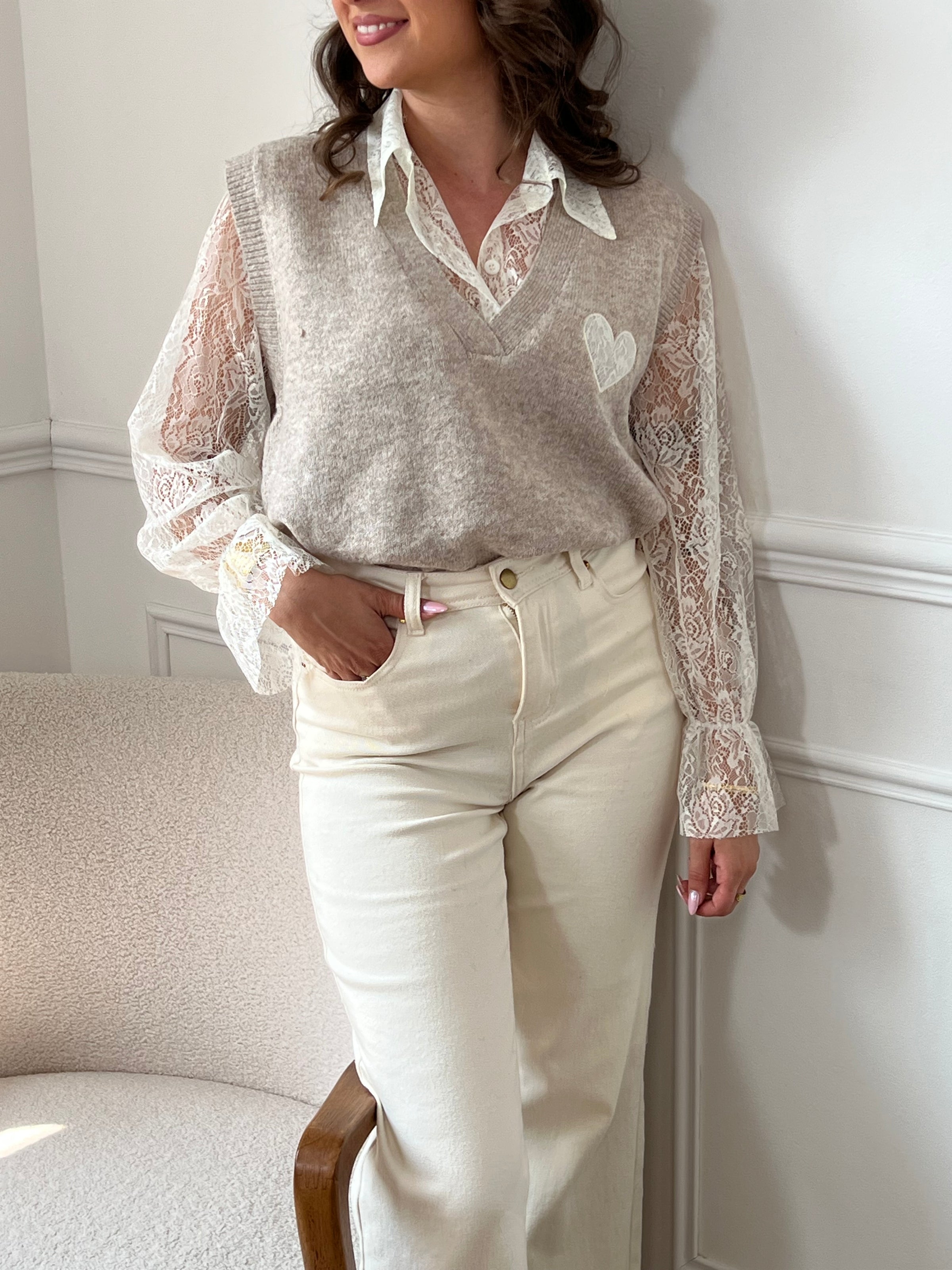 Le pull taupe Ayla associe élégance et confort avec son col en V classique. Il se porte avec un sous-pull en dentelle délicate, agrémenté de boutons sur toute la longueur pour une touche raffinée.