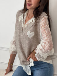 Le pull taupe Ayla associe élégance et confort avec son col en V classique. Il se porte avec un sous-pull en dentelle délicate, agrémenté de boutons sur toute la longueur pour une touche raffinée.