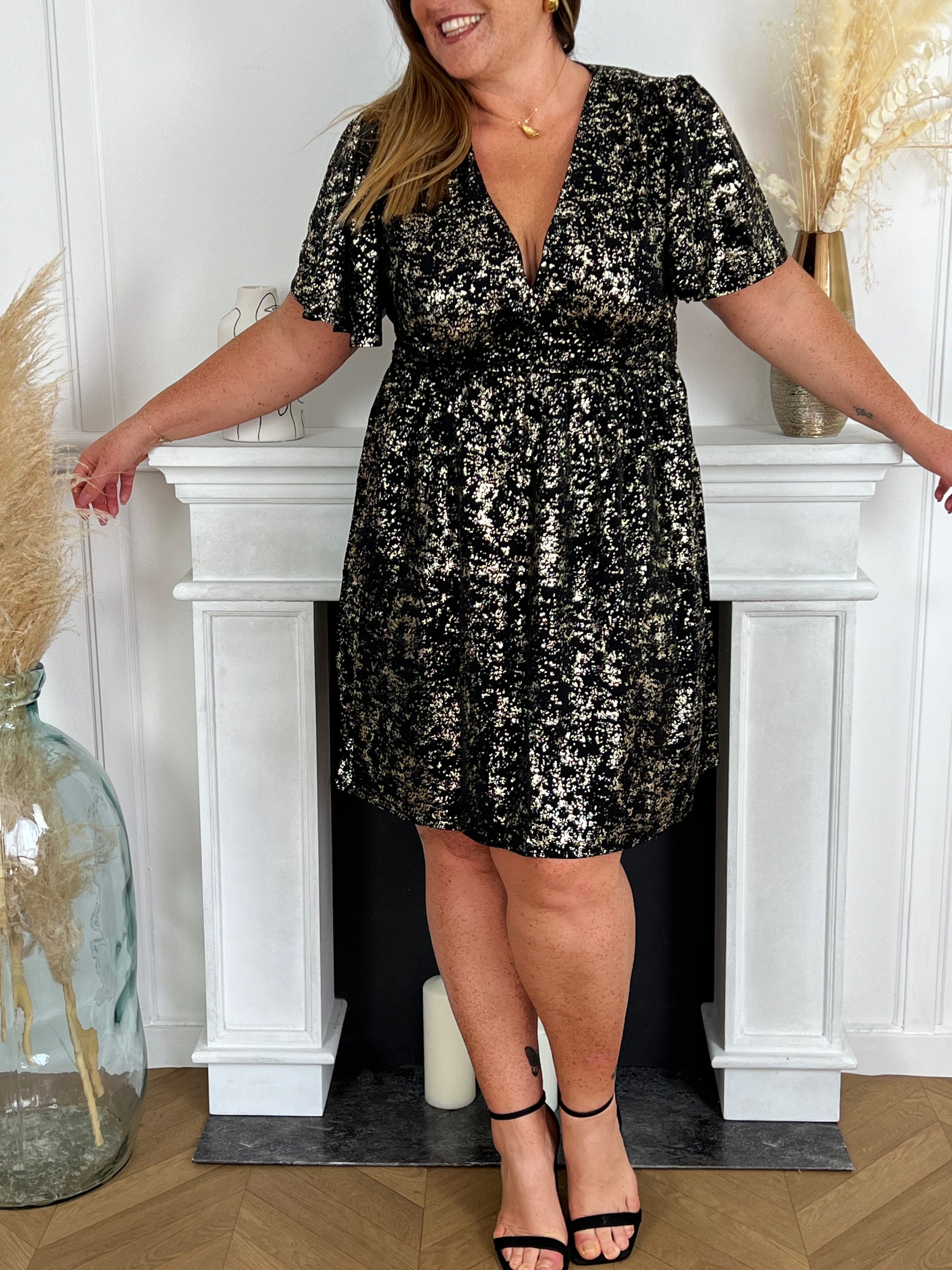 Une robe noire courte, délicatement ornée de détails dorés étincelants, incarne l'élégance subtile et le raffinement sophistiqué. Son tissu fluide épouse gracieusement les courbes, tandis que les accents dorés captent la lumière, ajoutant une touche de glamour à cette pièce intemporelle.