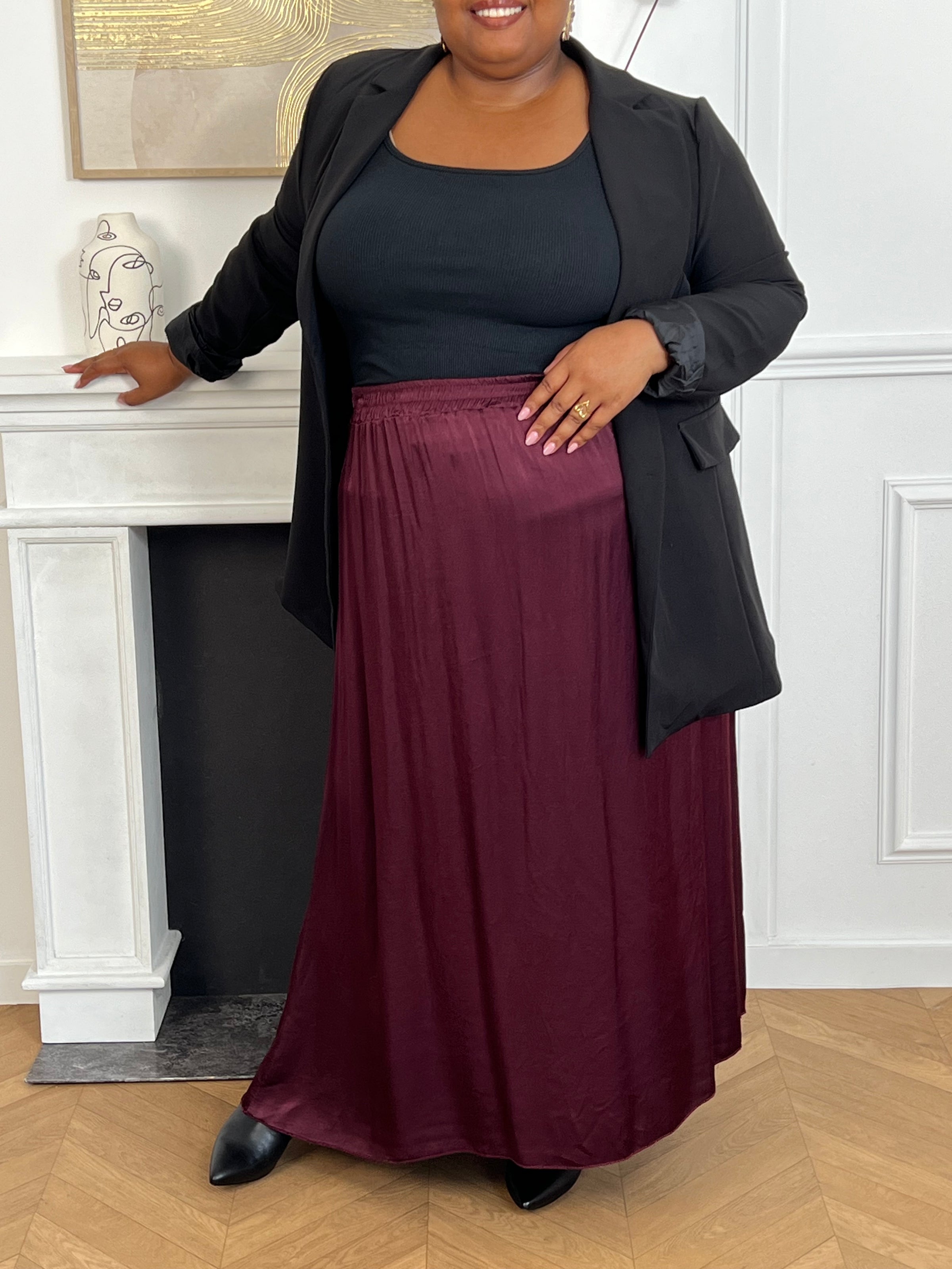 Cette jupe longue en satin bordeaux, modèle Lola, allie élégance et confort grâce à sa taille élastique qui s'adapte parfaitement à toutes les morphologies.