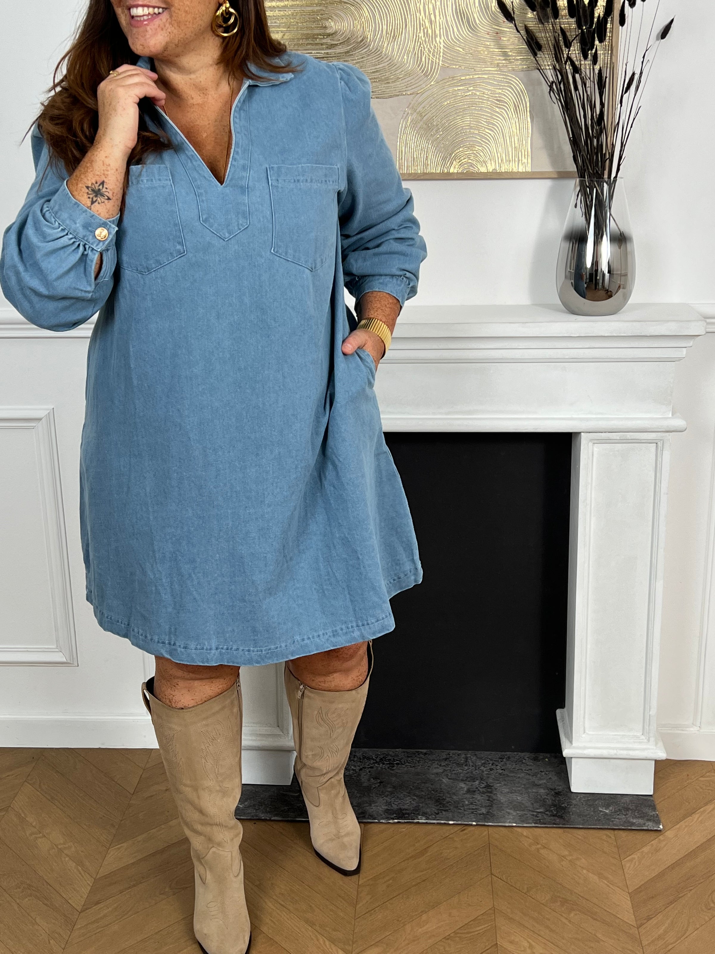 Cette robe courte en jean bleu clair séduit par sa coupe ample et son col V à revers. Dotée de manches longues, de poches pratiques et de détails dorés aux poignets, elle allie confort et style au quotidien.