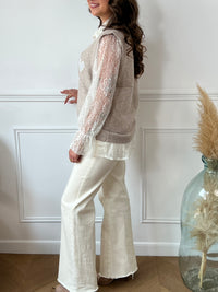 Le pull taupe Ayla associe élégance et confort avec son col en V classique. Il se porte avec un sous-pull en dentelle délicate, agrémenté de boutons sur toute la longueur pour une touche raffinée.