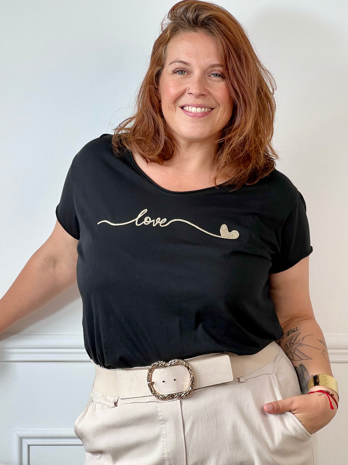 Tee-shirt noir grande taille pour femme, manches courtes et col V élégant. Sa coupe moderne plus longue à l’arrière offre confort et style. Détail chic : inscription dorée "Love". Couleurs tendance noir et doré, idéal pour un look casual et féminin