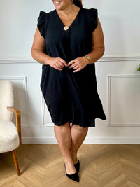 Cette robe noire sans manches, parfaite pour les grandes tailles, offre une silhouette élégante avec ses volants délicats aux épaules. Le col en V met en valeur le décolleté tandis que l'épingle dorée sur le devant ajoute une touche raffinée.