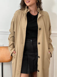 Trench beige femme avec ceinture, manches longues et col volanté pour une touche féminine. Boutons tout le long, doublure intérieure en carreaux vichy marron et écru, offrant élégance et confort. Coupe ample et deux poches latérales pratiques.
