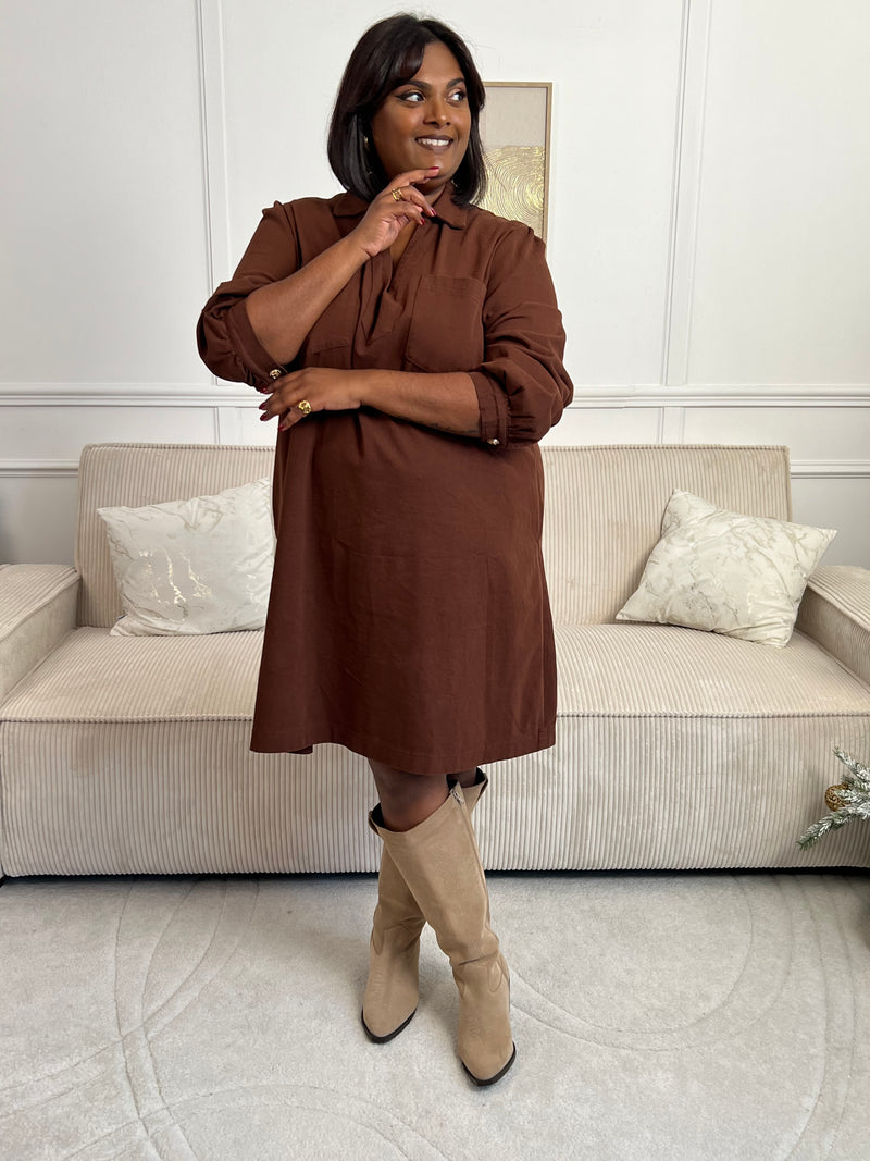 Cette robe courte en marron séduit par sa coupe ample et son col V à revers. Dotée de manches longues, de poches pratiques et de détails dorés aux poignets, elle allie confort et style au quotidien.