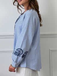 Cette blouse associe des rayures bleues et écrues élégantes à de délicats motifs floraux pour un look à la fois classique et féminin. Parfaite pour ajouter une touche de fraîcheur et de sophistication à votre tenue quotidienne.