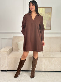 Cette robe courte en marron séduit par sa coupe ample et son col V à revers. Dotée de manches longues, de poches pratiques et de détails dorés aux poignets, elle allie confort et style au quotidien.