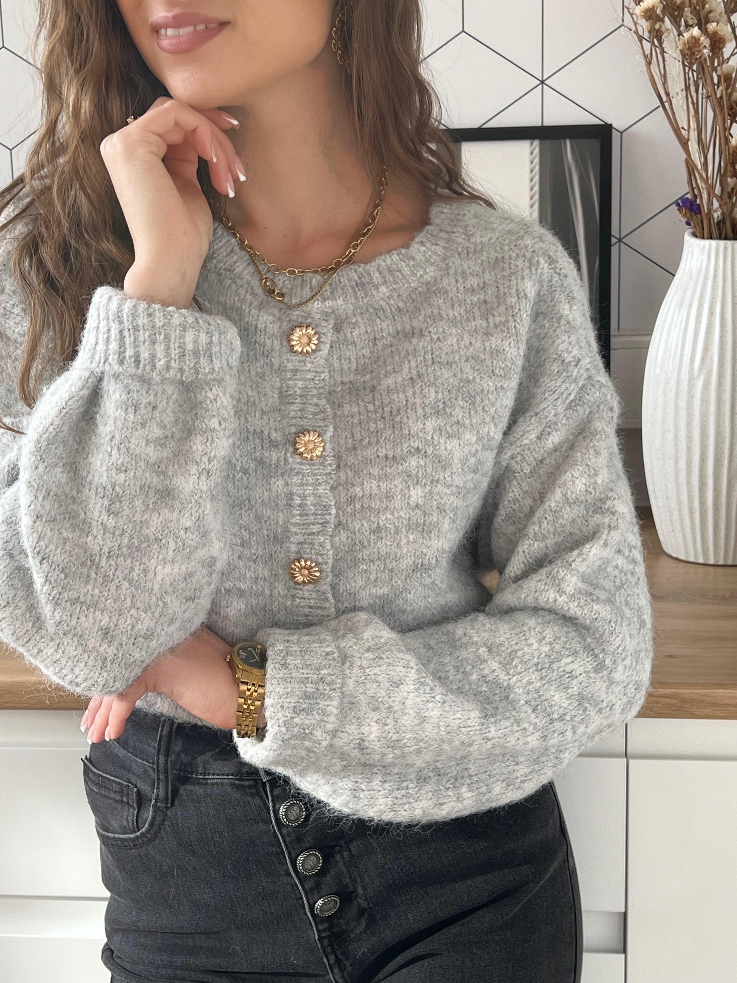 Ce pull gris Elisa est un incontournable pour votre garde-robe. Avec ses boutons dorés en forme de fleur au dos, il apporte une touche d'élégance et de fantaisie à votre tenue. 
