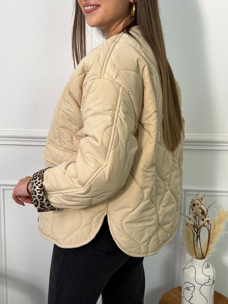 Cette veste matelassée beige, élégante et polyvalente, est conçue pour offrir confort et style à chaque saison. Dotée de manches longues et d'un col rond classique, elle présente une allure sophistiquée qui s'adapte à toutes les occasions. Fermée par des boutons sur toute la longueur, cette veste se distingue par ses détails soignés : une poche sur le devant pratique et des fentes latérales pour plus de fluidité et de confort. Son intérieur à imprimé léopard ajoute une touche audacieuse et tendance. 