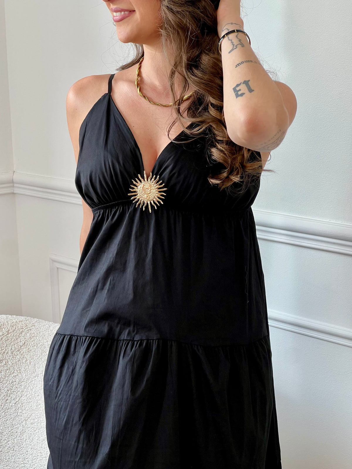 Cette robe longue noire, Elenora, allie élégance et confort grâce à ses bretelles réglables et sa taille élastique qui s’adaptent parfaitement à votre silhouette. Son col en V met en valeur le décolleté, tandis que le détail doré en forme de soleil apporte une touche lumineuse et raffinée sur la poitrine.
