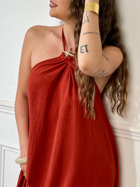 Adoptez une allure audacieuse avec cette robe longue terracotta Adeje. Son col montant réglable, orné d’un détail doré, apporte une touche sophistiquée tandis que l’élastique au dos assure un confort parfait. Sans manches et à la coupe ample, elle offre une liberté de mouvement idéale pour affirmer votre style avec assurance.&nbsp;