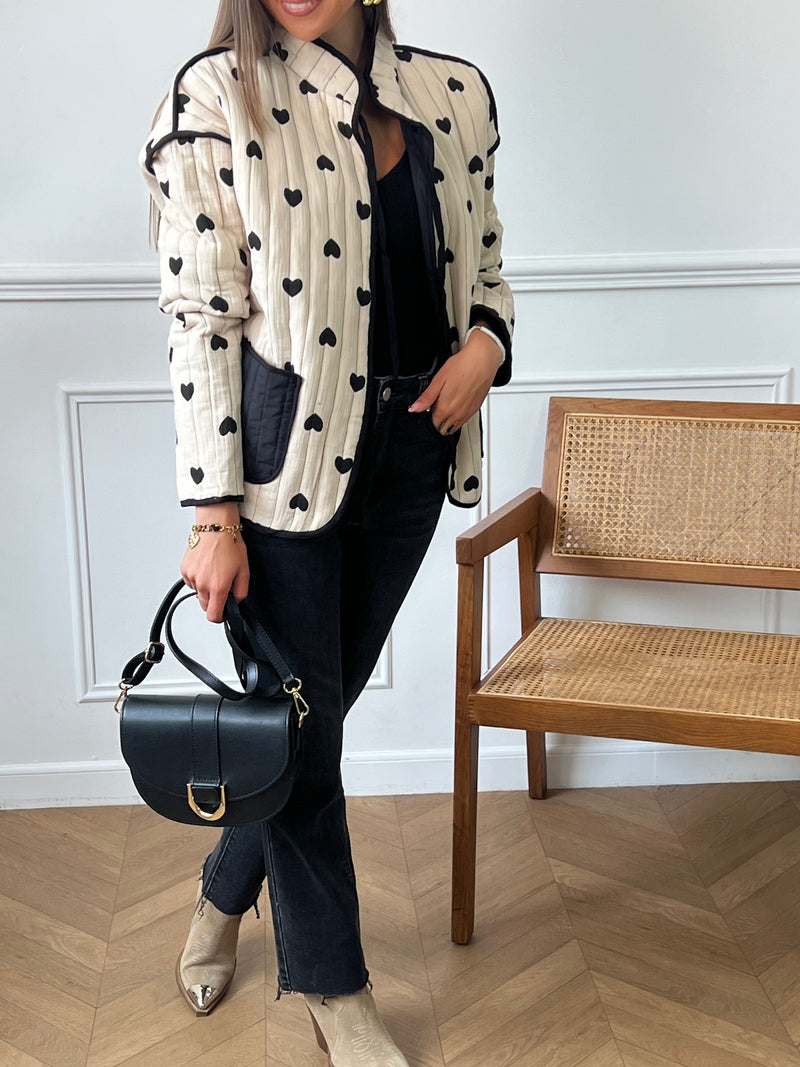 Découvrez notre veste matelassée en coton beige et noir "Joelie" avec des motifs coeurs noirs. Pratique avec ses 2 poches à l'avant, elle vous gardera au chaud avec ses manches longues et ses liens de serrage à l'avant. Ajoutez une touche de style à votre tenue grâce à ses couleurs intemporelles.