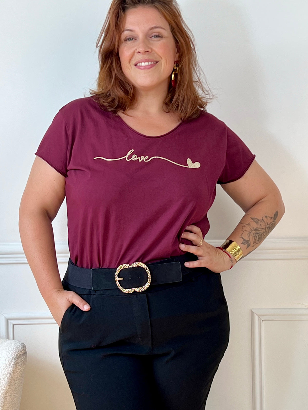 Tee-shirt bordeaux grande taille pour femme, manches courtes et col V élégant. Sa coupe moderne plus longue à l’arrière offre confort et style. Détail chic : inscription dorée "Love". Couleurs tendance bordeaux et doré, idéal pour un look casual et féminin