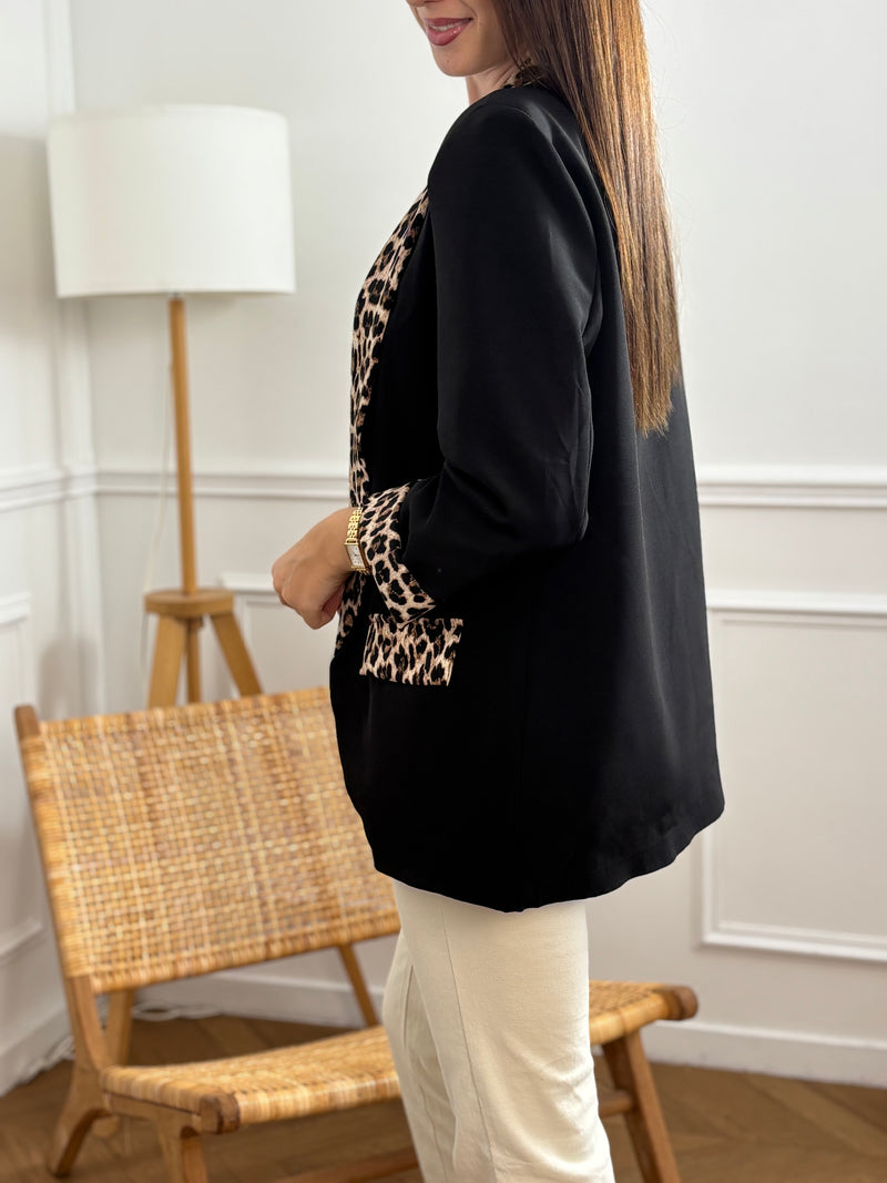 Ce blazer noir, nommé Axella, allie élégance et originalité. Ses manches longues et ses deux poches factices sur le devant offrent une silhouette structurée, tandis que le détail léopard qui court le long des poches et des revers de manches apporte une touche audacieuse et moderne.