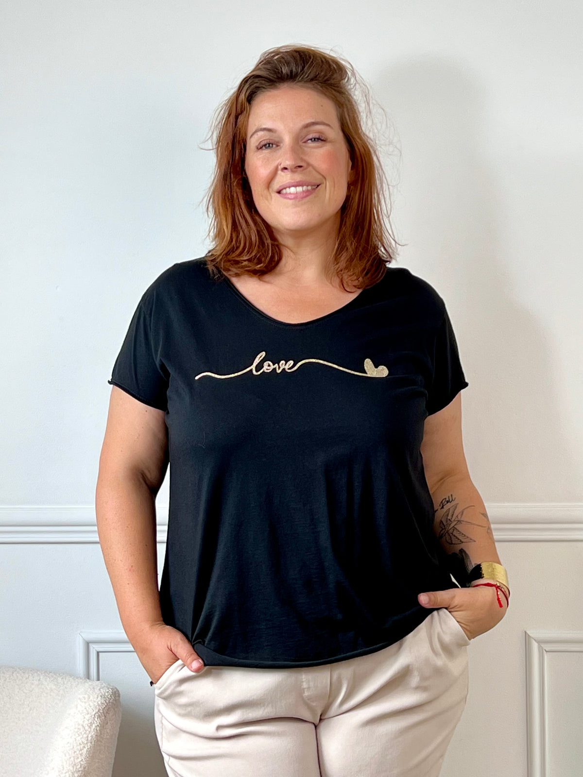 Tee-shirt noir grande taille pour femme, manches courtes et col V élégant. Sa coupe moderne plus longue à l’arrière offre confort et style. Détail chic : inscription dorée "Love". Couleurs tendance noir et doré, idéal pour un look casual et féminin