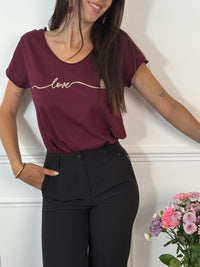 Ce tee-shirt bordeaux "Aliyah" allie confort et élégance avec ses manches courtes et son col rond classique. Sa touche distinctive, une inscription dorée sur le devant, apporte une subtile note de sophistication. Idéal pour un style décontracté mais soigné au quotidien.