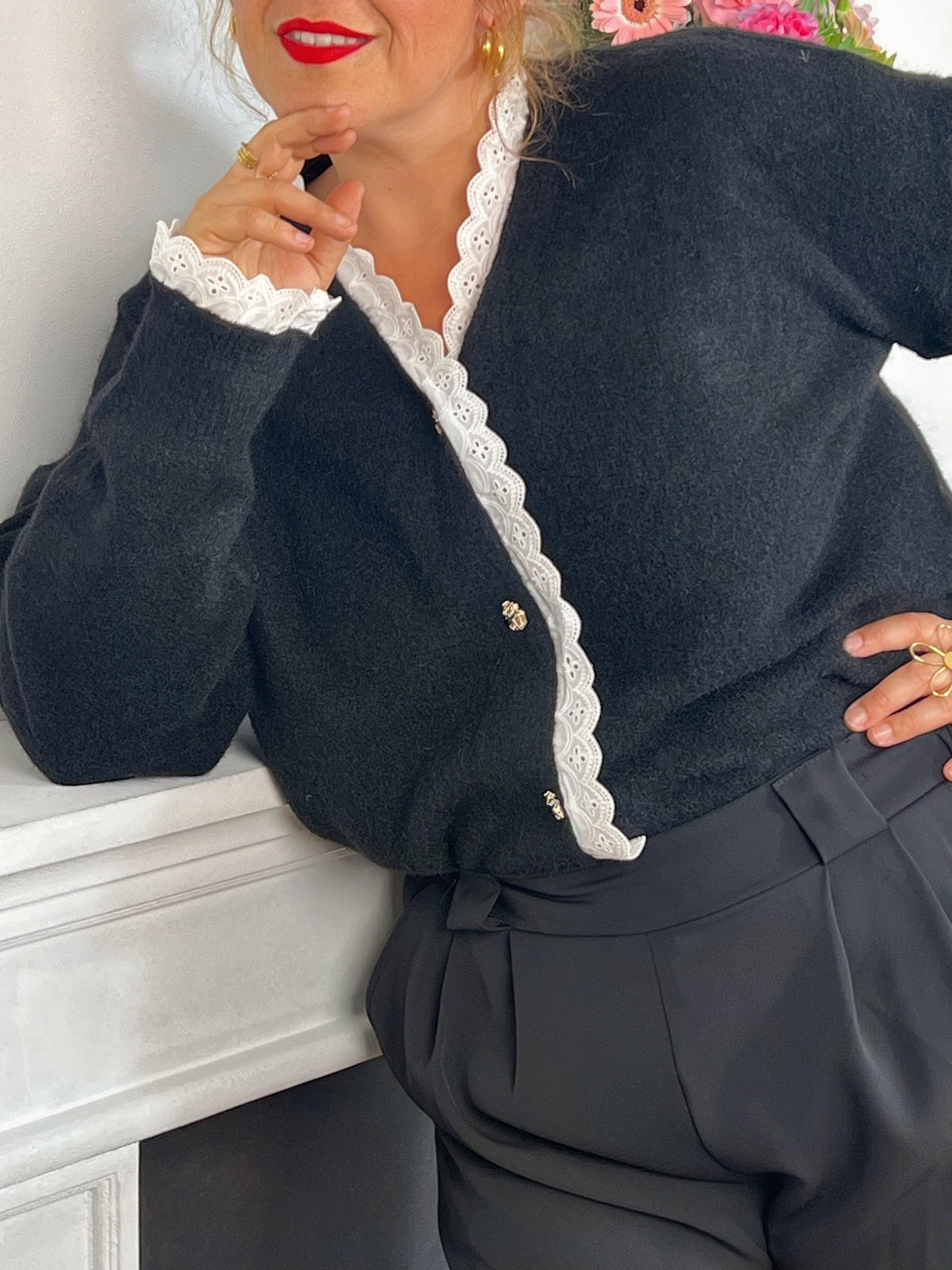 Pull noir élégant, orné de boutons argentés aux reflets dorés subtils. Le col et les poignets se distinguent par de délicats détails festonnés en écru, apportant une touche raffinée et contrastée.