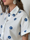 Découvrez notre chemise blanche et bleue : Jihane ! Avec ses manches courtes et sa broderie de fleurs bleues et blanches, cette chemise est à la fois élégante et décontractée. Ajoutez une touche de couleur à votre tenue tout en restant chic.