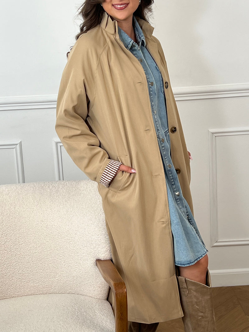 Trench beige femme avec ceinture, manches longues et col volanté pour une touche féminine. Boutons tout le long, doublure intérieure en carreaux vichy marron et écru, offrant élégance et confort. Coupe ample et deux poches latérales pratiques.