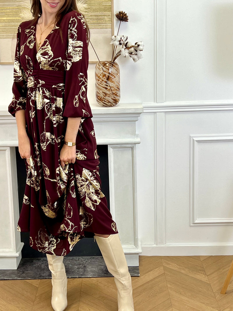 Robe longue bordeaux élégante aux détails dorés, idéale pour les occasions spéciales. Son col V et ses manches longues apportent une touche raffinée, tandis que l’élastique au dos assure un confort parfait. Entièrement doublée jusqu’à mi-longueur, elle allie style et aisance dans des nuances subtiles de bordeaux et doré.