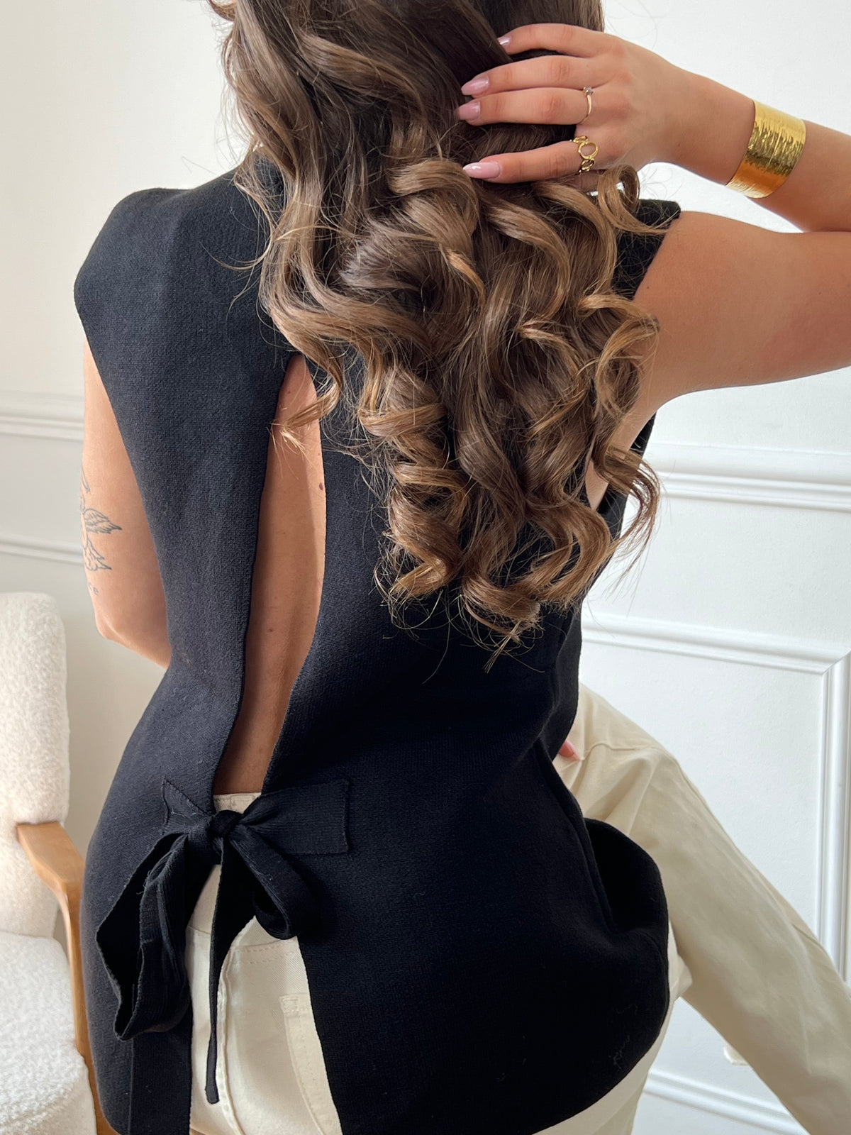 Ce gilet sans manches noir Rosalia offre une allure élégante grâce à ses boutons dorés alignés sur le devant. Son col en V et son dos nu avec lien à nouer apportent confort et féminité, parfaits pour compléter vos tenues estivales ou superpositions raffinées.