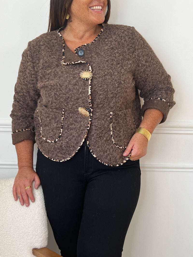 Chic et audacieuse, cette veste marron se démarque par son pourtour souligné d’une fine bande léopard, subtile touche de caractère. Pratique et élégante, elle est dotée de deux poches à l’avant et s’agrémente d’épingles amovibles dorées, offrant la possibilité de personnaliser votre look au gré de vos envies.