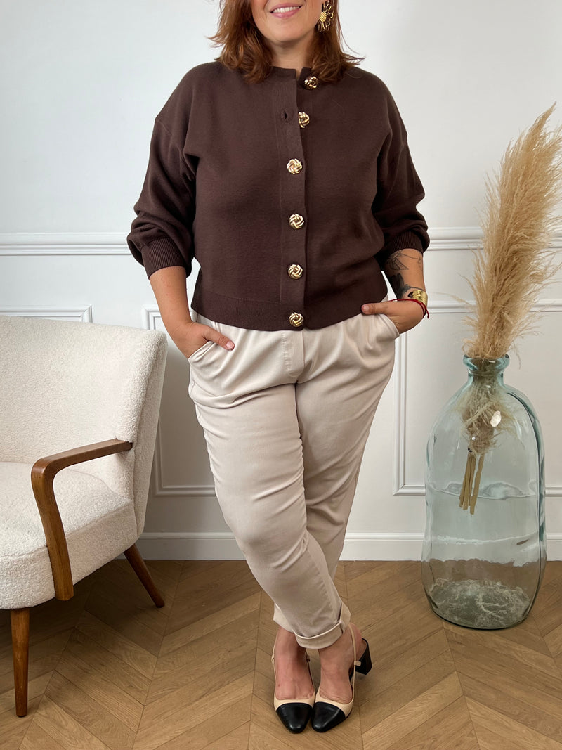 Ce gilet marron présente une coupe courte et féminine. Ses manches longues et son col rond offrent confort et élégance. Les boutons dorés sur le devant ajoutent une touche raffinée, tandis que l’étiquette discrète sur un côté souligne son authenticité.