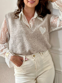 Le pull taupe Ayla associe élégance et confort avec son col en V classique. Il se porte avec un sous-pull en dentelle délicate, agrémenté de boutons sur toute la longueur pour une touche raffinée.