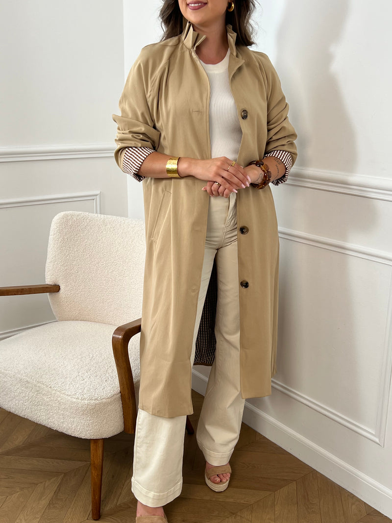 Trench beige femme avec ceinture, manches longues et col volanté pour une touche féminine. Boutons tout le long, doublure intérieure en carreaux vichy marron et écru, offrant élégance et confort. Coupe ample et deux poches latérales pratiques.