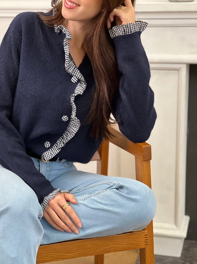 Élégance et originalité se rencontrent avec ce gilet bleu marine. Ses finitions à volants à carreaux au col, aux poignets, le long des boutons et sur toute la ligne apportent une touche raffinée et pleine de charme. Un essentiel revisité pour sublimer tes looks du quotidien.