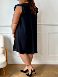 Cette robe noire sans manches, parfaite pour les grandes tailles, offre une silhouette élégante avec ses volants délicats aux épaules. Le col en V met en valeur le décolleté tandis que l'épingle dorée sur le devant ajoute une touche raffinée.