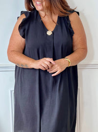 Cette robe noire sans manches, parfaite pour les grandes tailles, offre une silhouette élégante avec ses volants délicats aux épaules. Le col en V met en valeur le décolleté tandis que l'épingle dorée sur le devant ajoute une touche raffinée.
