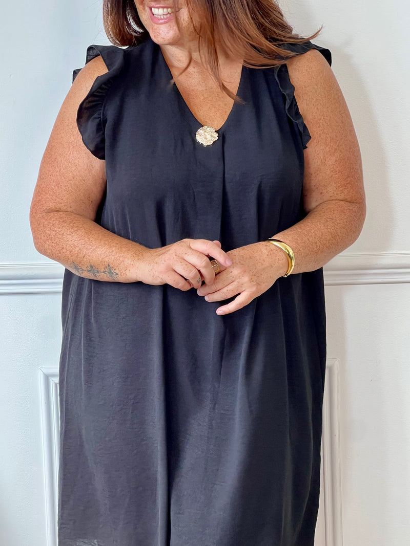 Cette robe noire sans manches, parfaite pour les grandes tailles, offre une silhouette élégante avec ses volants délicats aux épaules. Le col en V met en valeur le décolleté tandis que l'épingle dorée sur le devant ajoute une touche raffinée.