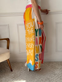 Ce pantalon en lin aux motifs colorés et inspirés des vacances respire la bonne humeur. Avec ses inscriptions comme "You are my Sunshine", "Lemoncello" ou "You are the Sunshine in everyday", il invite à la détente et à l’évasion. Ses teintes de beige, vert, orange, rose, rouge et bleu en font une pièce pétillante, idéale pour un look estival plein de charme et de légèreté.