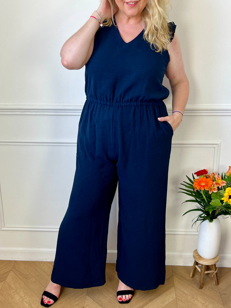 Cette combinaison longue bleue Curve : Liona, une pièce incontournable pour les femmes de grande taille. Avec son col V flatteur, sa taille élastique et son dos nu élégant, elle est à la fois pratique et chic. Ses poches latérales et volants aux épaules ajoutent une touche de style. Disponible en bleu marine et noire