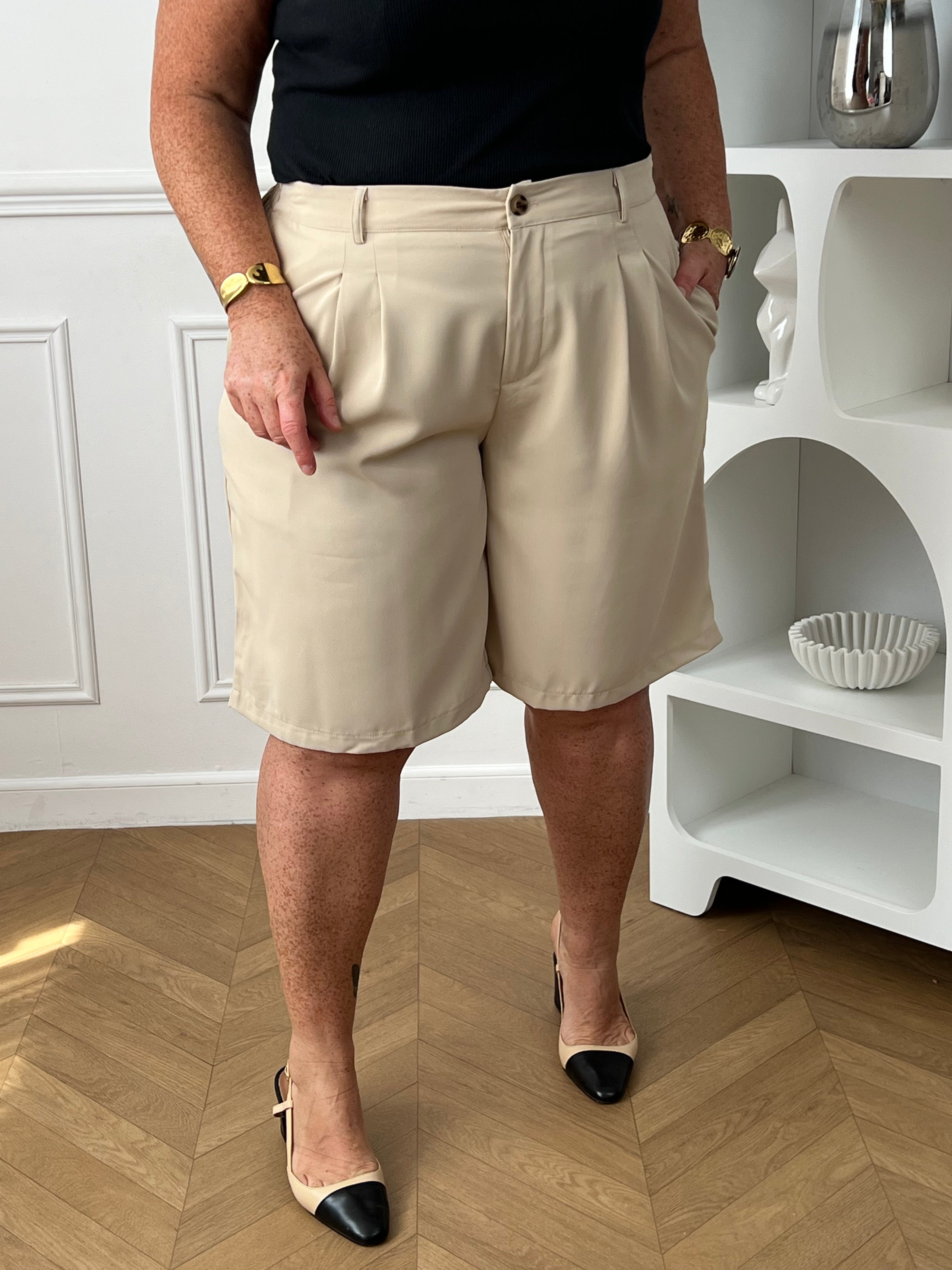 Bermuda beige grande taille pour femme, alliant confort et style pour la saison estivale. Équipé de deux poches latérales pratiques, d’une taille élastique au dos et de passants pour ceinture, il assure un ajustement parfait. Sa fermeture avec bouton et zip garantit un bon maintien. Polyvalent et facile à assortir, ce bermuda taupe est un indispensable du dressing casual chic.