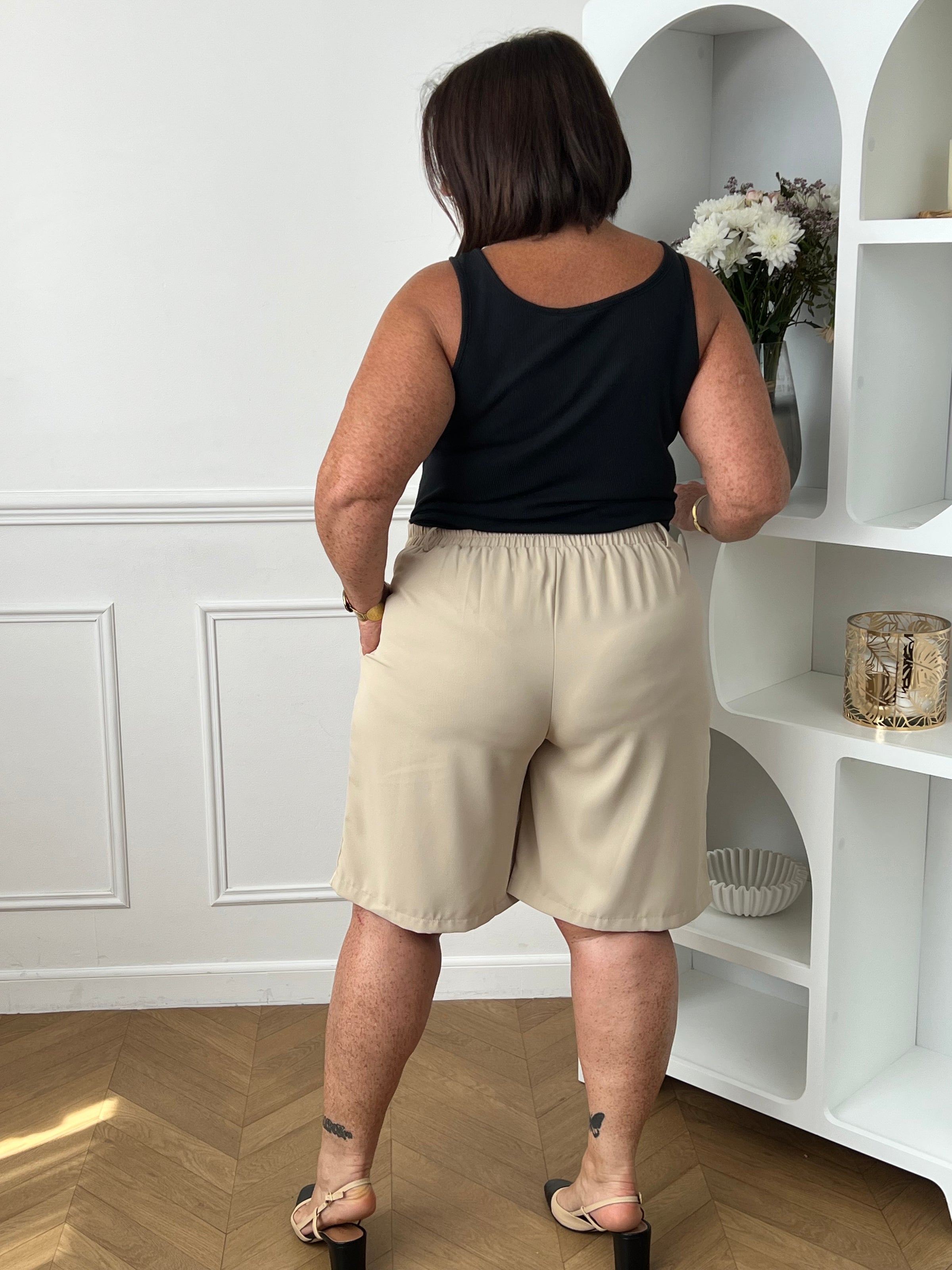 Bermuda beige grande taille pour femme, alliant confort et style pour la saison estivale. Équipé de deux poches latérales pratiques, d’une taille élastique au dos et de passants pour ceinture, il assure un ajustement parfait. Sa fermeture avec bouton et zip garantit un bon maintien. Polyvalent et facile à assortir, ce bermuda taupe est un indispensable du dressing casual chic.