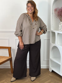 Blouse à carreaux Nour grande taille portée de face avec un pantalon large foncé, montrant sa coupe ample et ses manches retroussées.