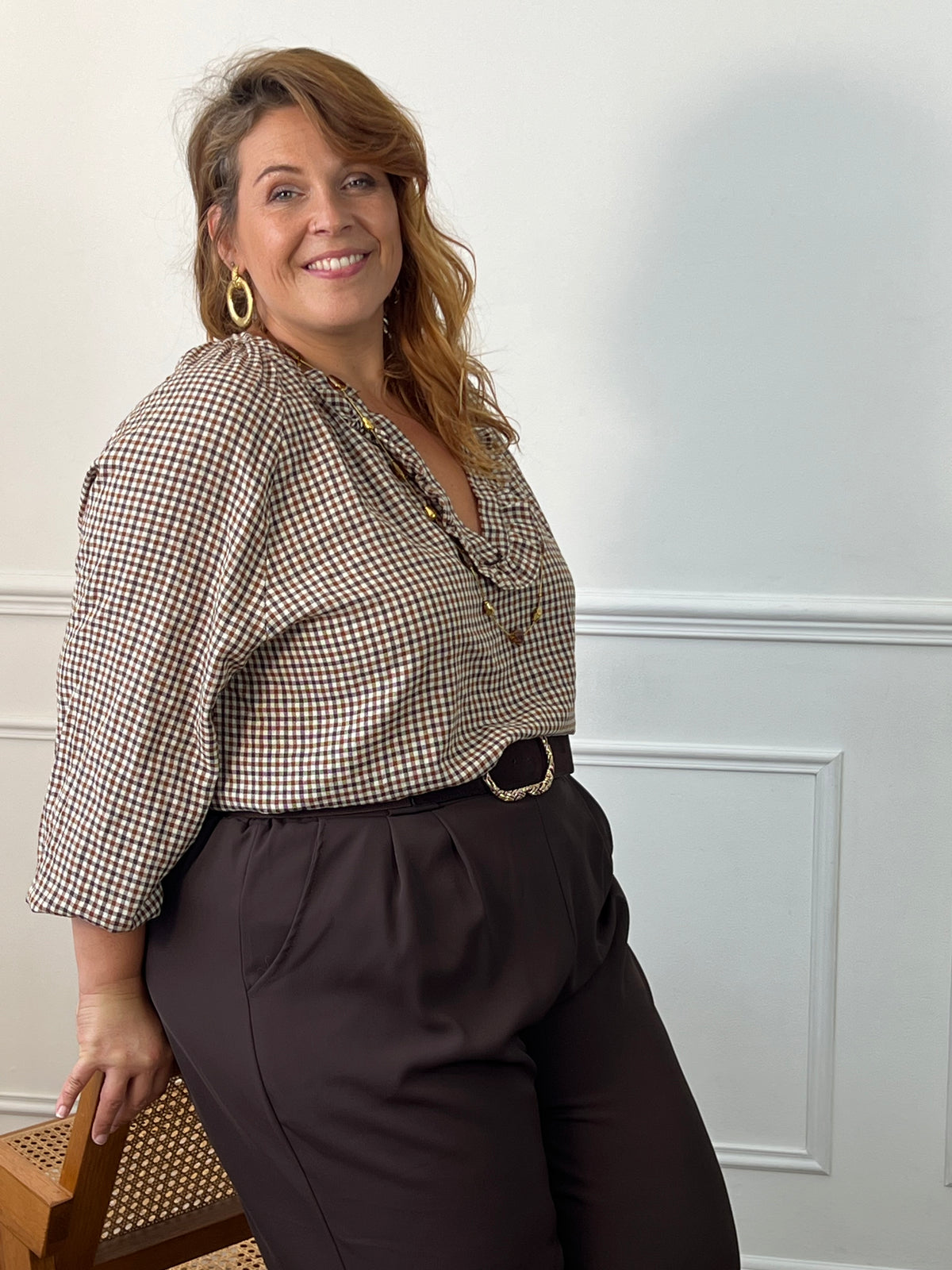 Vue de trois-quarts de la blouse Nour à carreaux, rentrée dans un pantalon foncé avec une ceinture à boucle dorée.