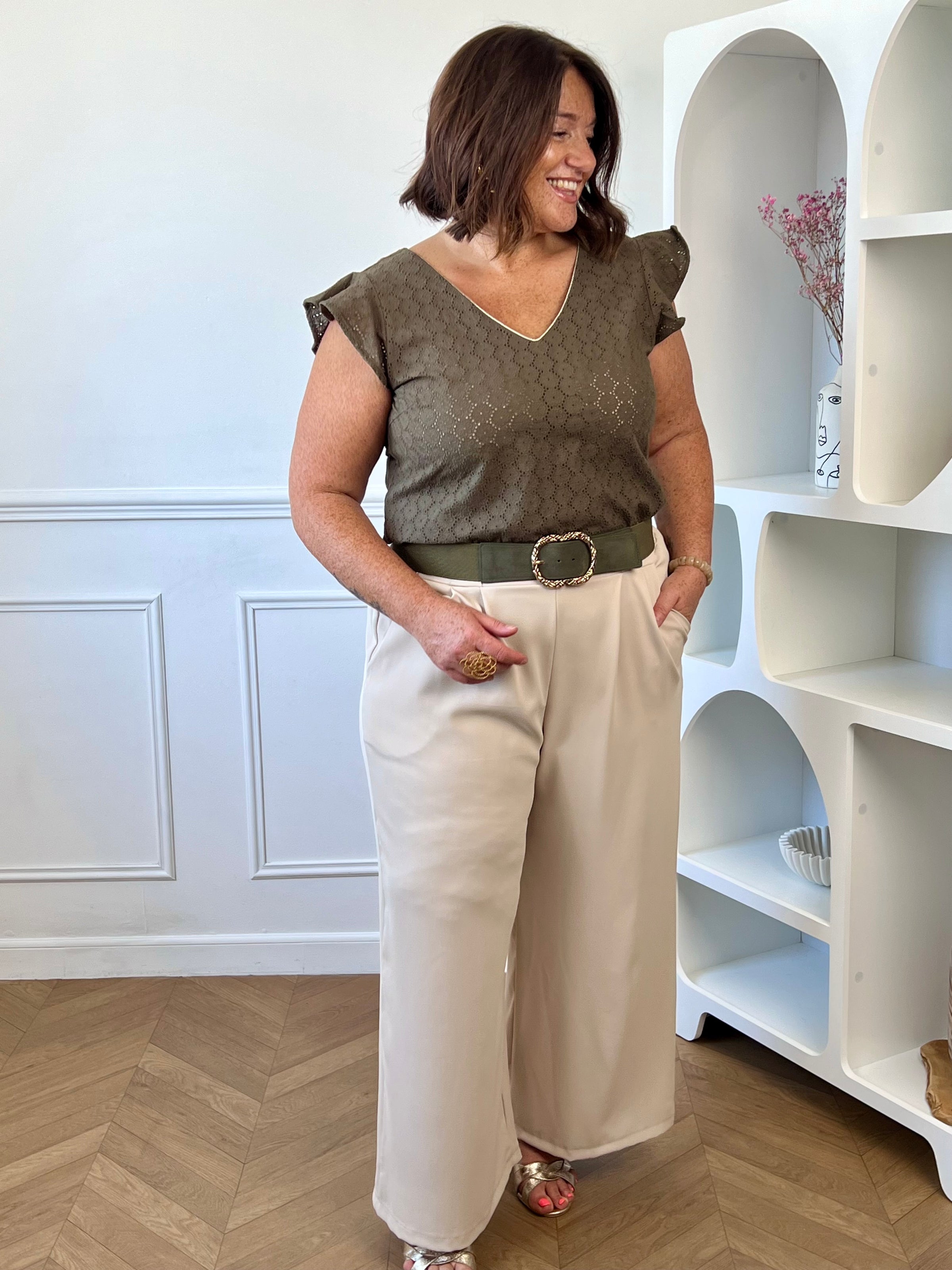 Blouse kaki féminine avec volants aux épaules et détail doré à l’avant.