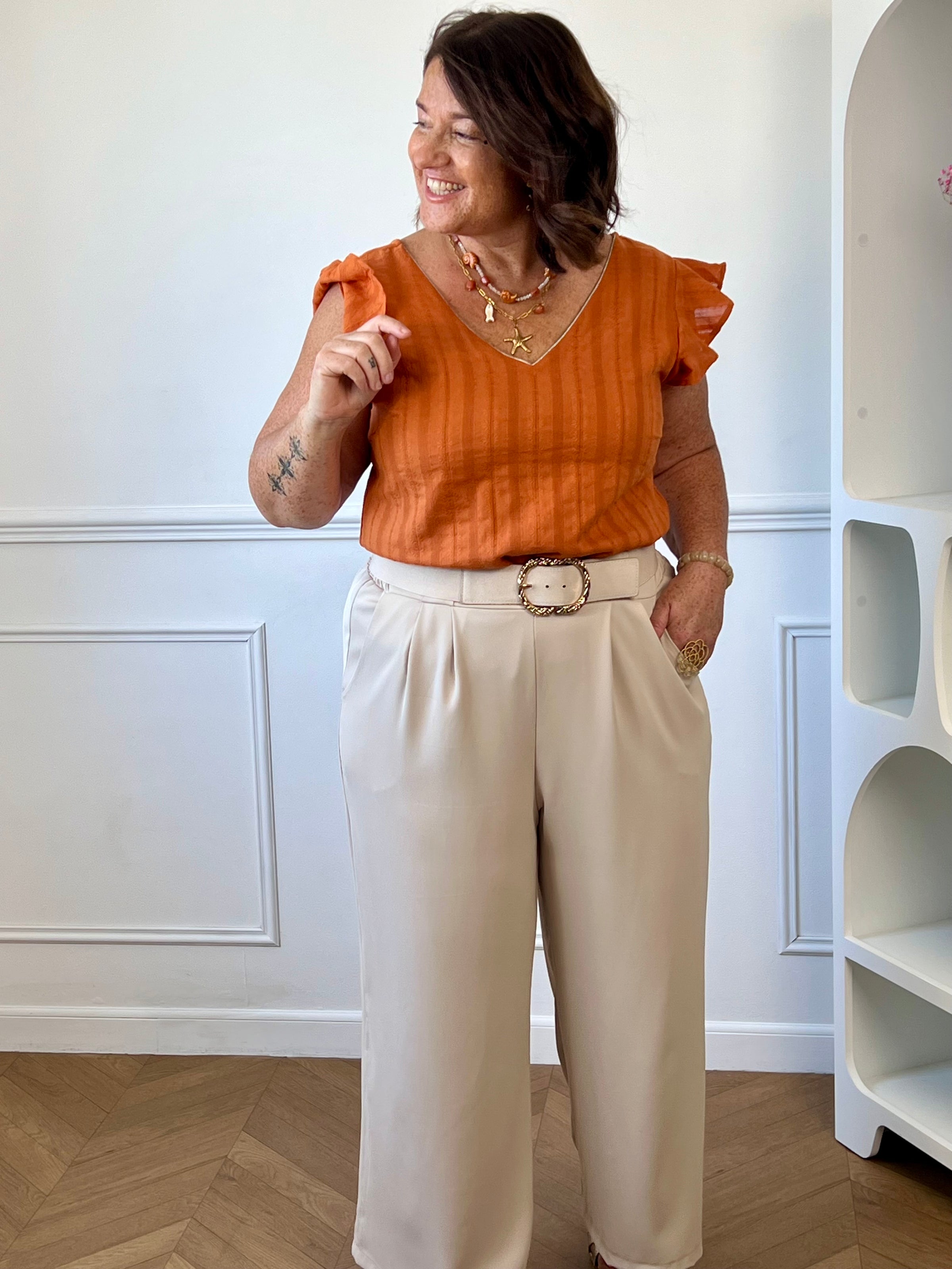 Vue de dos de la blouse orange en coton avec col V, lien de serrage et petits boutons.
