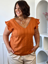 Blouse orange et dorée grande taille femme avec col V, broderie ajourée et volants aux épaules.