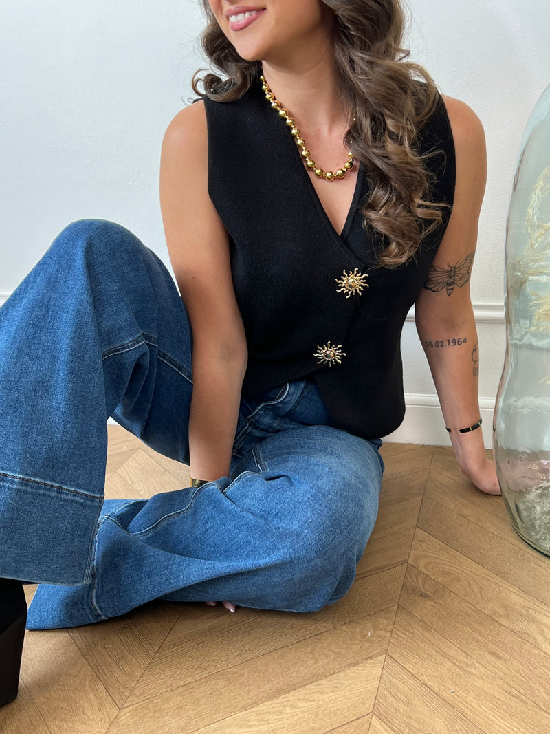 Ce gilet sans manches noir, nommé Elvire, allie élégance et originalité. Sa fermeture à boutons sur toute la longueur est sublimée par un détail doré en forme de soleil, apportant une touche lumineuse à votre tenue. Son col en V flatteur met en valeur votre silhouette, tandis que sa coupe sans manches offre confort et liberté de mouvement.