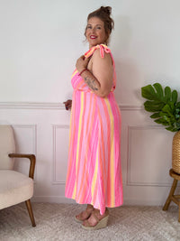 Plongez dans un tourbillon de couleurs avec cette robe longue sans manches, aux teintes vibrantes de rose, orange et jaune. Ses nœuds factices aux épaules ajoutent une touche de charme, tandis que sa coupe fluide en fait une pièce légère et joyeuse, parfaite pour les beaux jours.&nbsp;