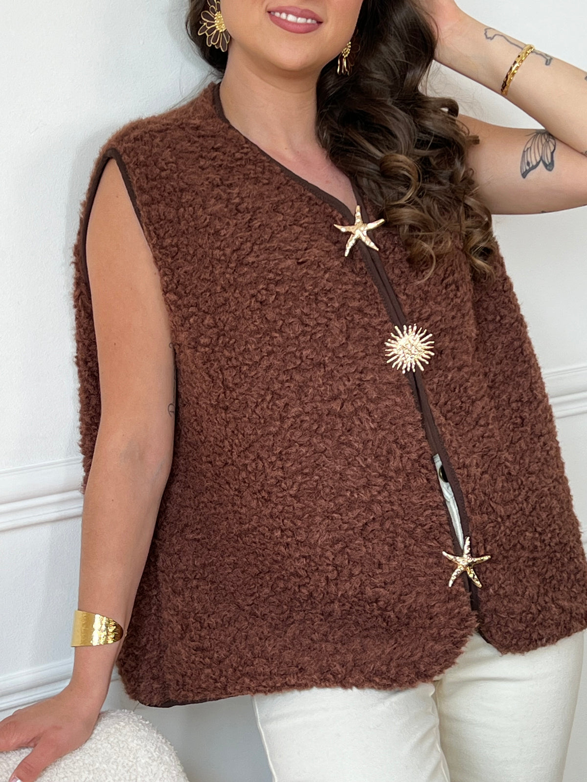 La veste moumoute sans manches Eda allie douceur et style. Conçue pour offrir un confort optimal, elle présente un col en V élégant et des broches dorées délicates sur le devant, qui ajoutent une touche sophistiquée.