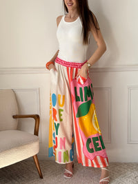 Ce pantalon en lin aux motifs colorés et inspirés des vacances respire la bonne humeur. Avec ses inscriptions comme "You are my Sunshine", "Lemoncello" ou "You are the Sunshine in everyday", il invite à la détente et à l’évasion. Ses teintes de beige, vert, orange, rose, rouge et bleu en font une pièce pétillante, idéale pour un look estival plein de charme et de légèreté.