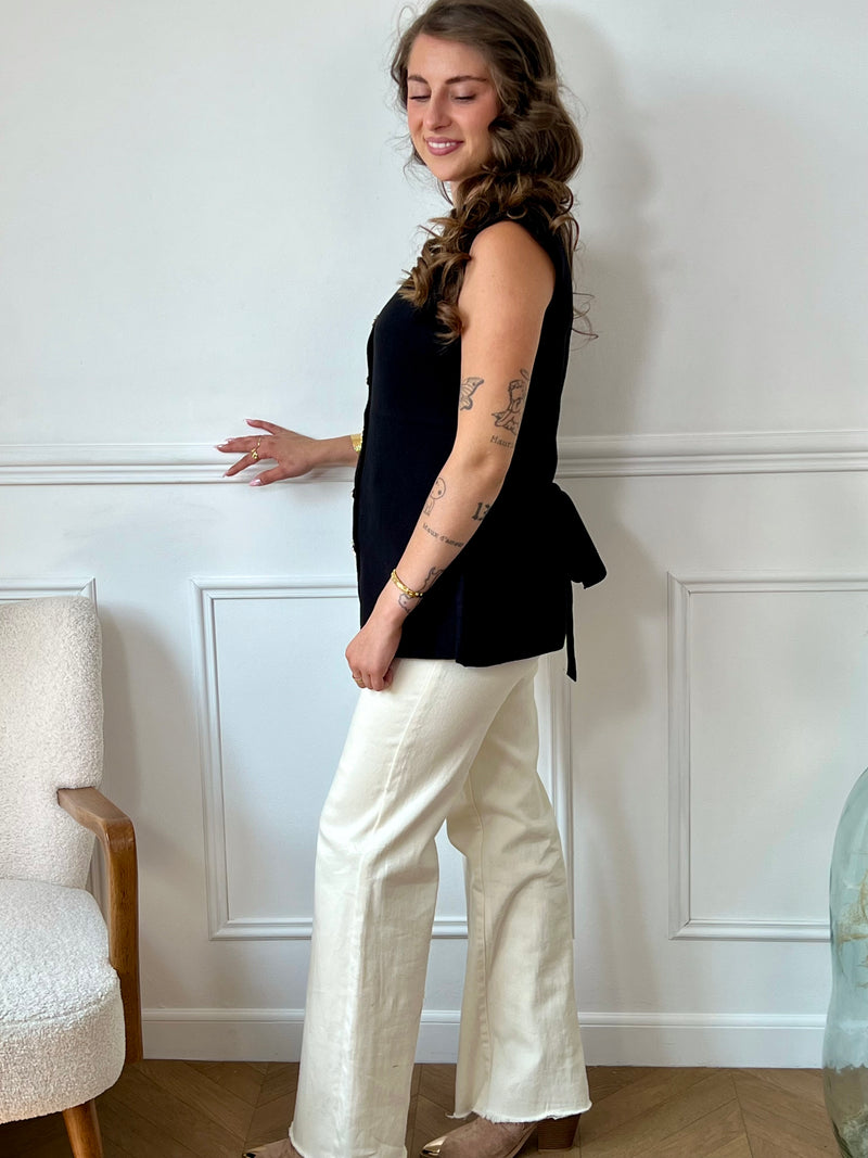 Ce gilet sans manches noir Rosalia offre une allure élégante grâce à ses boutons dorés alignés sur le devant. Son col en V et son dos nu avec lien à nouer apportent confort et féminité, parfaits pour compléter vos tenues estivales ou superpositions raffinées.