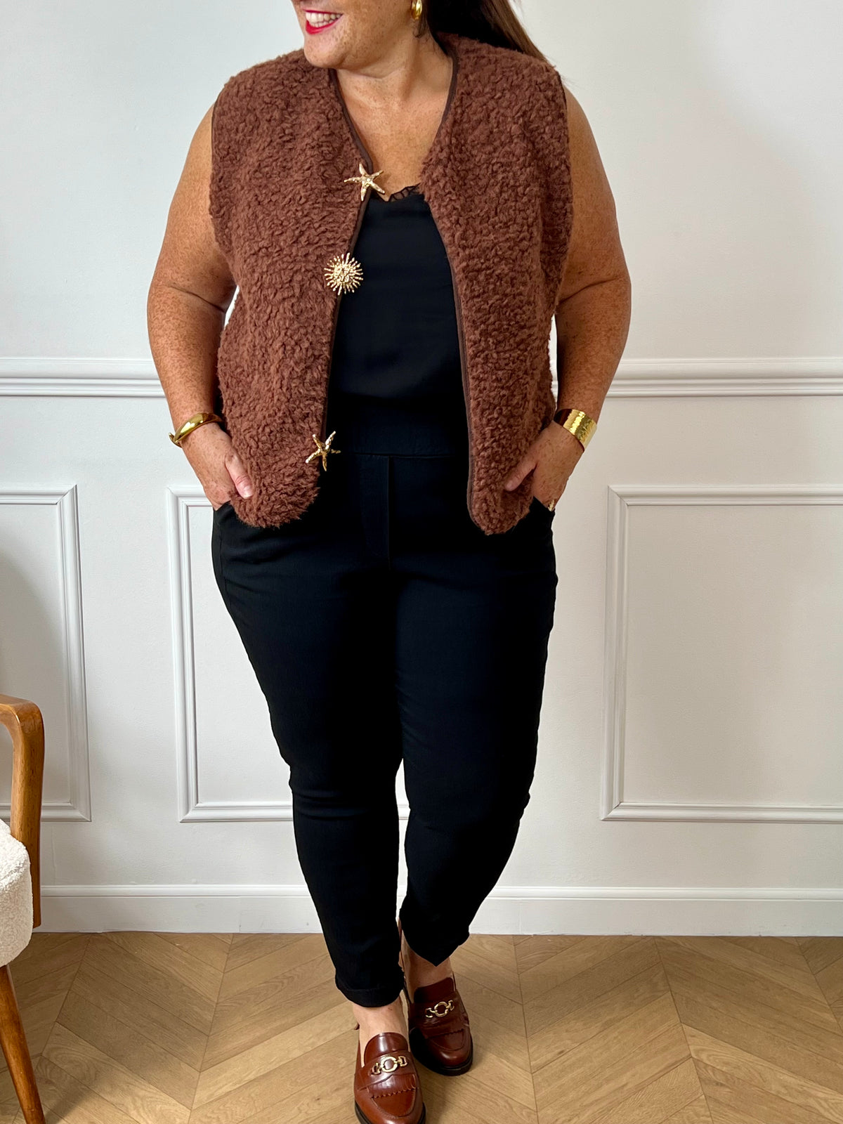 La veste moumoute sans manches Eda allie douceur et style. Conçue pour offrir un confort optimal, elle présente un col en V élégant et des broches dorées délicates sur le devant, qui ajoutent une touche sophistiquée.